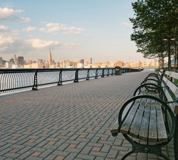 Scenic Eclipse vor der Skyline von New York City, helle Uferpromenade mit Bänken, Baumreihen und grauen Pflastersteinen, Abendlicht reflektiert auf dem Wasser Kanada-Rundreise