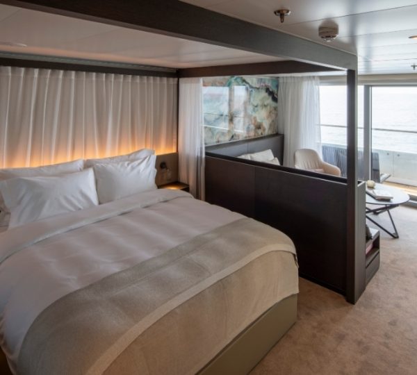 Luxuriöse Kabine auf Scenic Eclipse mit weißer Bettwäsche, warmen LED-Lichtlinien, großem Bett, separatem Wohnbereich und Meerblick, Hudson Bay Route Kanada-Rundreise