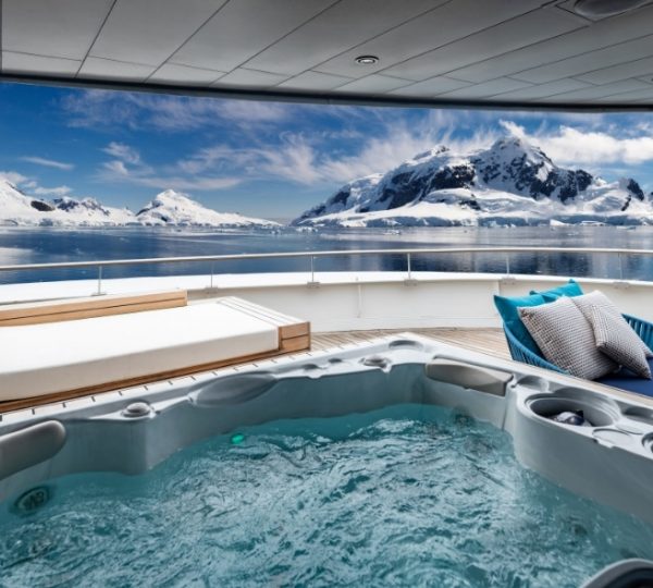 Whirlpool auf dem Luxuskreuzfahrtdeck der Scenic Eclipse mit türkisfarbenem Wasser, umliegende schneebedeckte Berglandschaft und hölzerne Loungemöbel Kanada-Rundreise