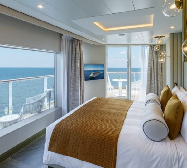 Zimmer mit Meerblick auf dem Kreuzfahrtschiff NCL Encore in Alaska; Balkontür geöffnet, Bett mit brauner Decke, moderne Innenausstattung und Aussicht aufs Meer Kanada-Rundreise
