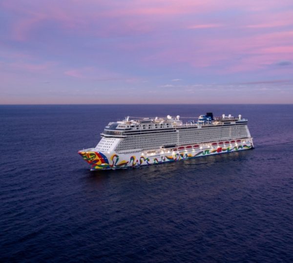 NCL Encore Kreuzfahrtschiff, bunt bemalt am Bug, treibt auf dem offenen Meer vor Alaska, pinker Abendhimmel und ruhiges tiefblaues Wasser im Hintergrund Kanada-Rundreise