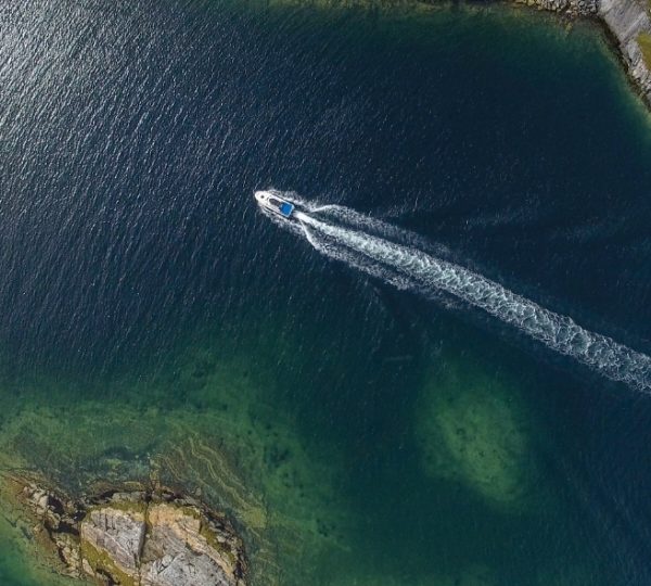 Boot zieht eine weiße Wasserlinie hinter sich, liegt auf tiefblauem Wasser vor einer felsigen Küstenlinie bei Battle Harbour in Newfoundland, Kanada Kanada-Rundreise