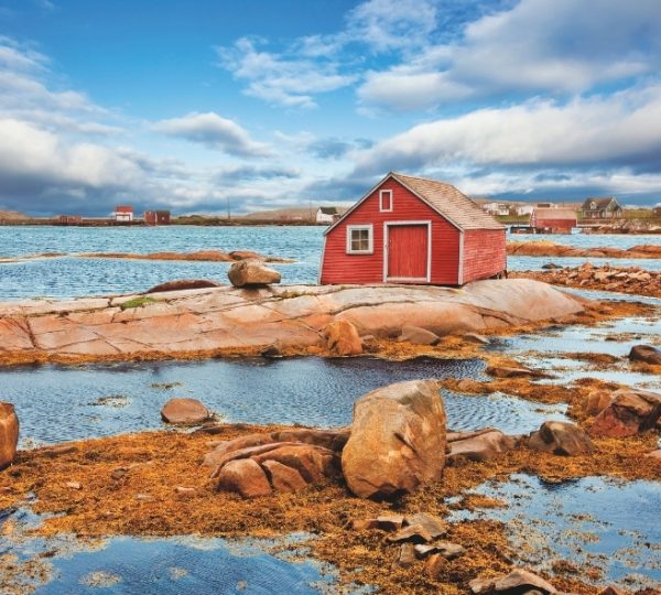 Rotes Fischerhaus auf Fogo Island vor einer felsigen Küstenlandschaft mit ruhigem Meer und blaugrauem Himmel, inspiriert von Atlantik-Kanada Kanada-Rundreise
