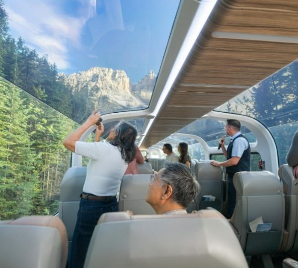 Rocky Mountaineer Passagiere schauen durch ein großes Panoramafenster auf eine imposante Berglandschaft, während Reisende an einer Vancouver- und Alaska-Kreuzfahrt teilnehmen Kanada-Rundreise
