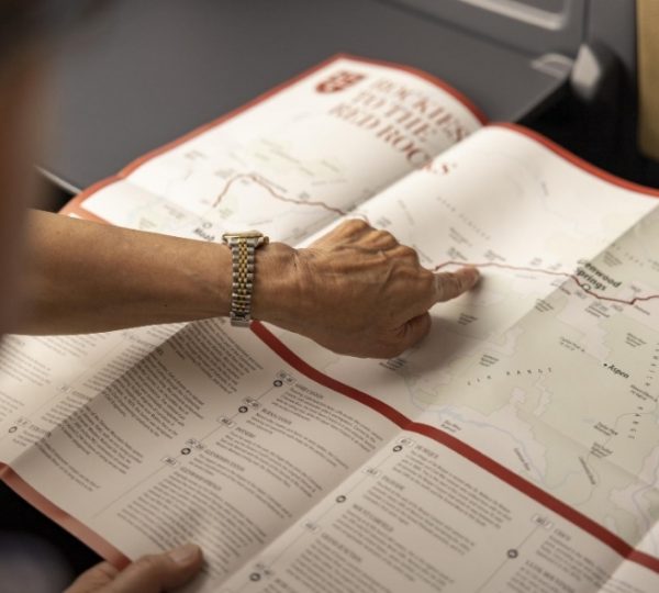 Rocky Mountaineer Reisetitel und Reiseführer: Eine Hand mit goldfarbenem Metallarmband zeigt auf eine detaillierte Karte im Reiseführer zur Vancouver- und Alaska-Kreuzfahrt im Rocky Mountaineer-Layout Kanada-Rundreise