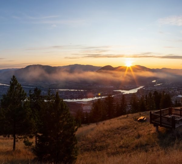 Rocky Mountaineer - Sonnenuntergang über eine bergige Landschaft mit Fluss, Wald und einer Holzplattform als Aussichtspunkt in Kanada bei Dämmerlicht Kanada-Rundreise