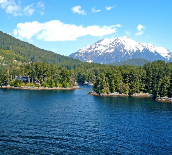 Landschaft am Rocky Mountaineer entlang eines blauen Sees mit bewaldeten Inseln und schneebedeckten Bergen, im Hintergrund Bergkette und klare Wolken am Himmel, geeignet für Kanada-Reisen Kanada-Rundreise