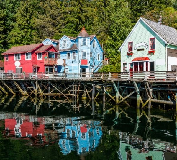 Rocky Mountaineer Reiseroute: bunte Holzhäuser auf Pfählen am Wasser, farbenfrohe Fassaden und eine Holzbrücke, aufgenommen während einer Vancouver-/Alaska-Reise Kanada-Rundreise