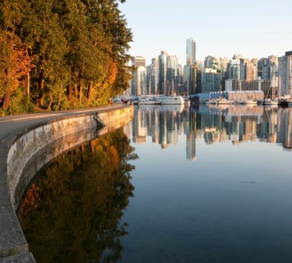 Rocky Mountaineer Aussicht auf Vancouver Hafen mit Uferpromenade, Wasserreflexion, Wolkenkratzer-Skyline und Marina‑Boote bei ruhigem Wetter Kanada-Rundreise