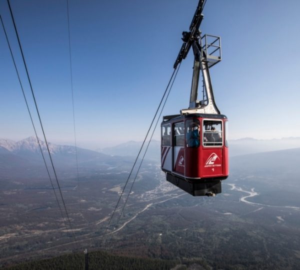 Rote Rocky-Mountaineer-Gondelbahn hängt über einer weitläufigen Berglandschaft mit Fluss und Wald, aufgenommen während einer Vancouver- und Alaska-Kreuzfahrt, panoramaartige Bergkette im Hintergrund Kanada-Rundreise