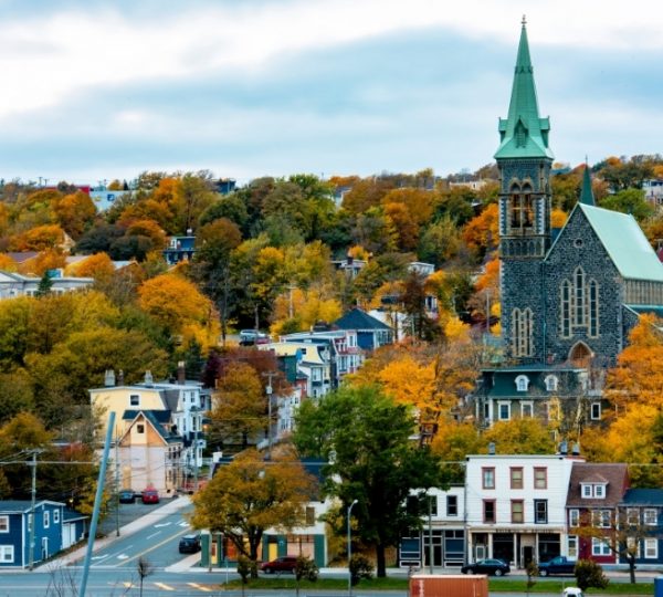 St.-Johns Herbstfarben-Ansicht einer gotischen Kirche in einer ostkanadischen Küstenstadt, umgeben von bunten Herbstbäumen und charmanten Häusern am Straßenrand Kanada-Rundreise