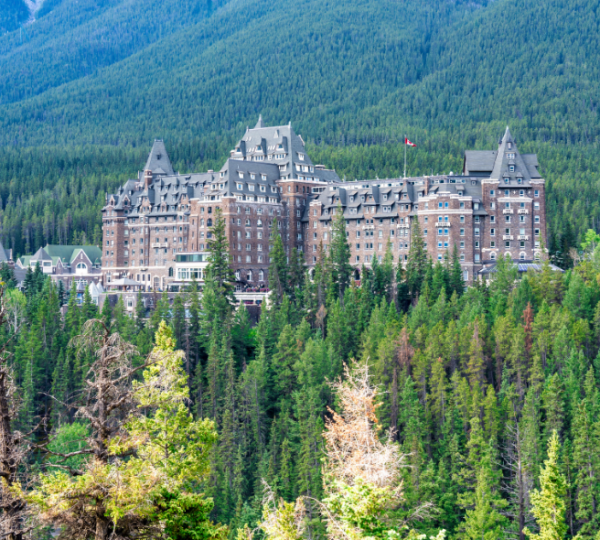 Großes graues Hotel im Wald von Banff Nationalpark, Banff Springs Hotel, umgeben von dichten Nadelwäldern und Bergen im Hintergrund Kanada-Rundreise