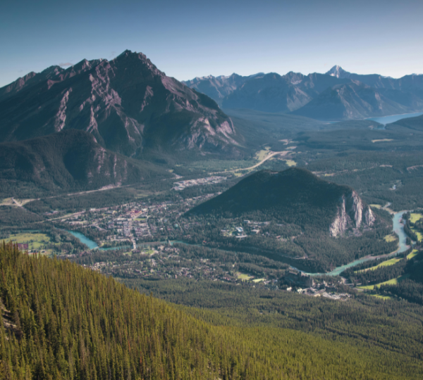 Banff Berglandschaft mit tiefem Tal, fließendem Fluss, grünen Waldflächen im Vordergrund und imposanten Gebirgszügen im Hintergrund; Panoramaaufnahme aus kanadischer Gebirgsregion Kanada-Rundreise