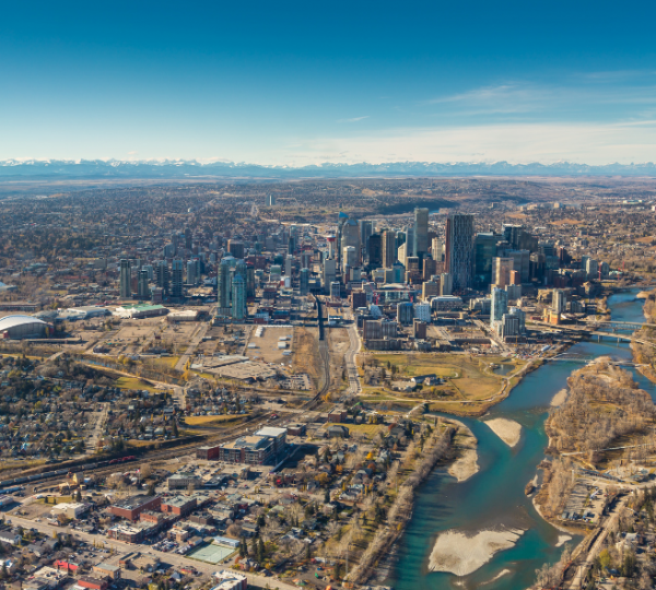 Luftaufnahme der Calgary-Skyline mit Flusslauf, Brücken und umliegenden Vororten unter blauem Himmel, stadtnahen Gebäuden und grünen Bereichen Kanada-Rundreise