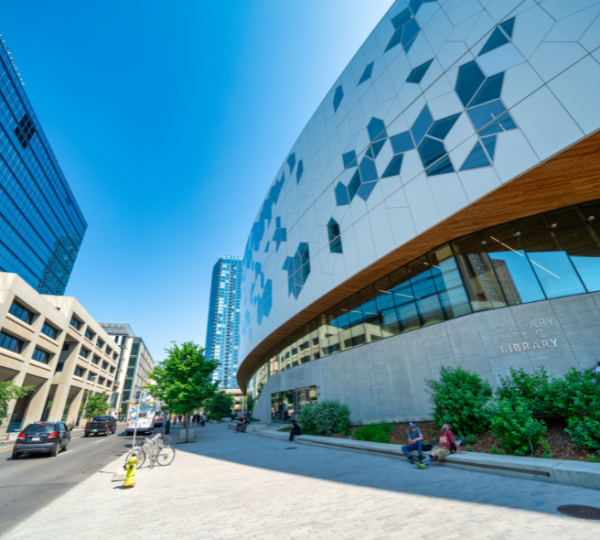 Blick auf die Calgary Public Library und umliegende moderne Gebäude mit blauer Himmel, klare Linien, Glasfassaden und Gehwege, Straßenszene mit wenigen Passanten Kanada-Rundreise