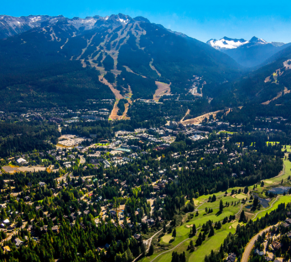 Whistler: Luftaufnahme einer bergigen Landschaft mit dichten grünen Wäldern, Talflächen und Siedlungen am Hang, ergänzt durch eine klare blaue Himmelsszene in Kanada Kanada-Rundreise