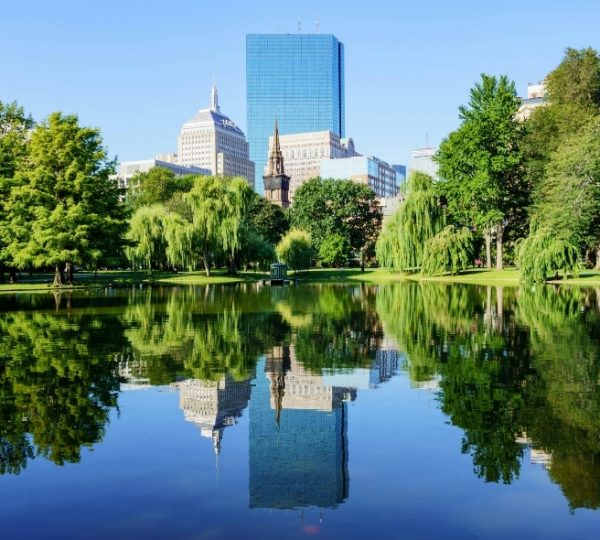Städtische Parklandschaft in Boston mit Teich, umgeben von grünen Bäumen und modernen Wolkenkratzern unter klarem Himmel, Boston im Hintergrund Kanada-Rundreise