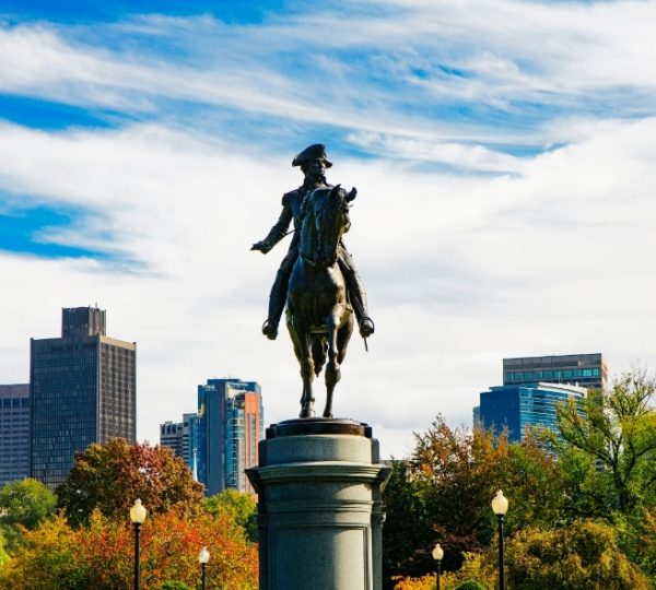Boston bronzenes Reiterstandbild vor einer modernen Skyline, umgeben von Herbstbäumen in Orange- und Grüntönen, zentral positioniert Kanada-Rundreise