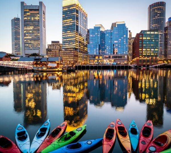 Boston Skyline am Hafen im Abendlicht spiegelt sich im ruhigen Wasser; bunte Kajaks im Vordergrund prägen das Bild mit moderner Stadtsilhouette Kanada-Rundreise