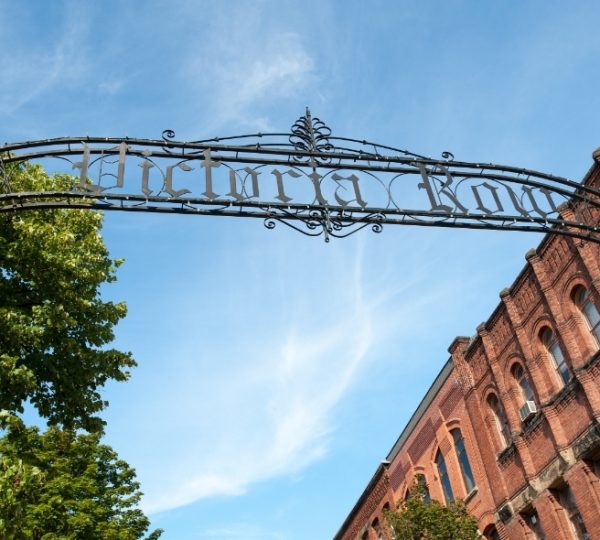 Charlottetown, Prince Edward Island: Blick auf eine elegante Backsteinfassade mit grünen Bäumen und einem schmiedeeisernen Tor unter blauem Himmel. Kanada-Rundreise
