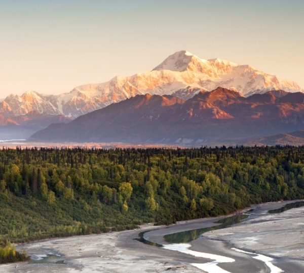 Denali-Nationalpark in Alaska mit schneeigen Gipfeln, dichter Waldlandschaft im Vordergrund und einem fließenden Flusslauf; majestätische Bergkulisse im Abendlicht Kanada-Rundreise