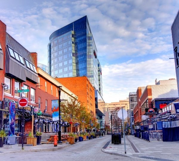 Halifax-Westküsten-Stadtbild mit modernen Glashochhäusern neben historischen Backsteinfassaden, belebte Straße, Straßencafés, Bäume und klare Wolken am Himmel Kanada-Rundreise