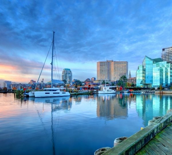 Halifax Hafenpanorama mit Segelboot, ruhigem Wasser, reflektierenden Glasgebäuden und einer städtischen Kulisse unter blauem Himmel Kanada-Rundreise