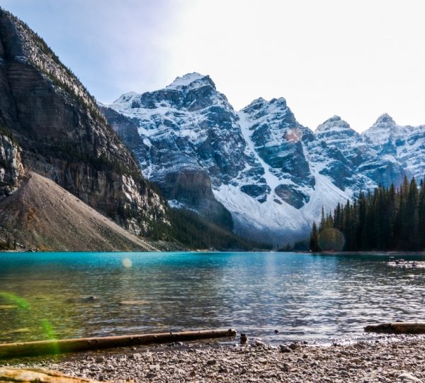 Türkisfarbener Bergsee vor schneebedeckten Berggipfeln; Ufer mit Kies, Wald rechts; Bergkette im Hintergrund erinnert an Banff/Jasper–Canada Strong Pass 2026 Kanada-Rundreise