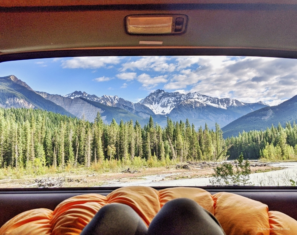 Blick aus dem Autofenster auf eine grüne Waldlandschaft mit schneebedeckten Berggipfeln im Hintergrund; Parks Canada, Canada Strong Pass 2026, Banff/Jasper Kanada-Rundreise