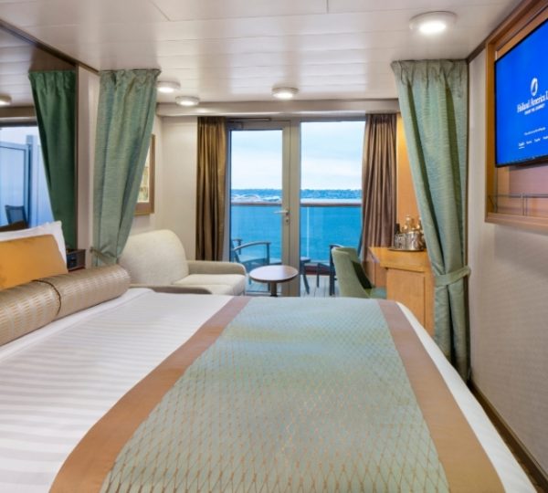 Zwei Doppelbetten in einer eleganten Kabine der Zuiderdam mit Blick aufs Meer durch große Fenster, TV an der Wand, grüne Vorhänge und dekorativer Bettüberwurf Kanada-Rundreise