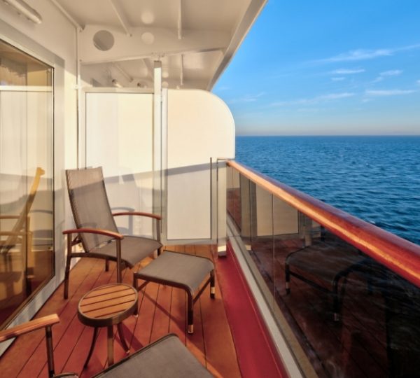Blick vom Balkon der Zuiderdam auf das weite Meer, Holzdeck, Glasgeländer und klaren Himmel; ikonischer Kreuzfahrtkomfort an Bord der Holland America Line Kanada-Rundreise