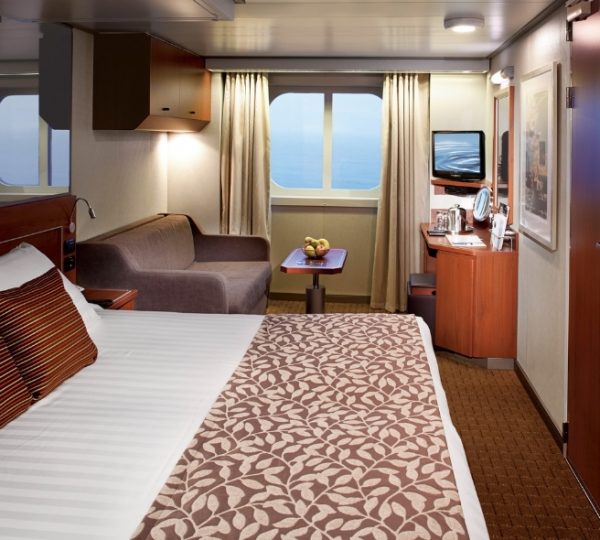 Kabine auf der Nieuw Amsterdam Kreuzfahrtschiff mit braunen Akzenten, gemütliches Bett, Sofa, kleiner Tisch, Obstkorb, Meerblickfenster, Moderne Holzmöbel von Holland America Line Kanada-Rundreise
