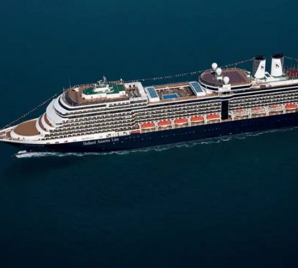 Die Nieuw-Amsterdam von Holland America Line gleitet durch das blaugrüne Wasser; ein großes Kreuzfahrtschiff mit weißer Oberseite, dunklem Rumpf und vielen Decks inside passage