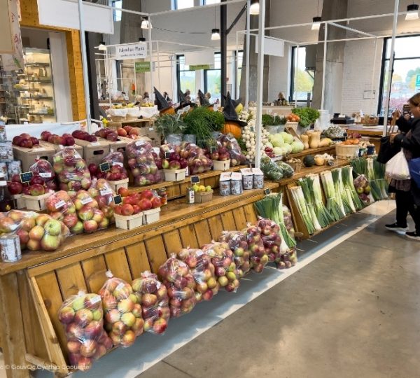 Bunter Marktstand mit frischem Obst und Gemüse in Quebec: Äpfel, Paprika, Kürbis, Zwiebeln und Kräuter auf Holzregalen, ergänzt durch Lauch. Kanada-Rundreise