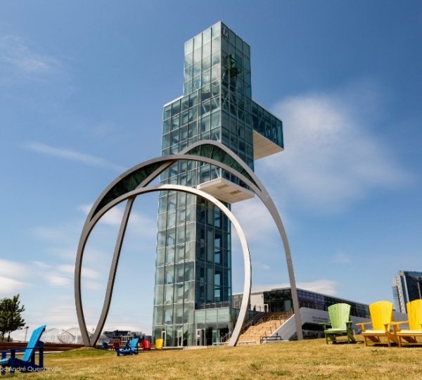 Vor einer glasverkleideten Architektur in Montréal steht die Skulptur „Leurs effigies“ von Yann Po creau, umrahmt von metallischen Bögen und bunten Stühlen. Kanada-Rundreise