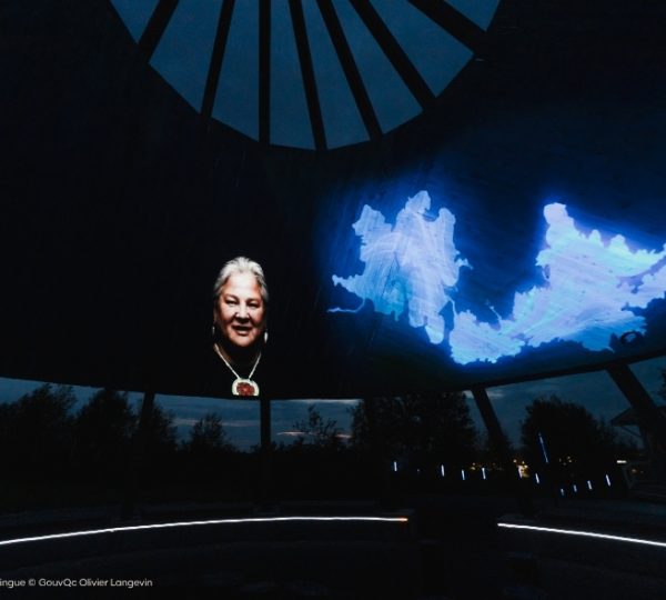 Dunkles Tipi mit blauer, projizierter Landkarte über der Kuppel, im Hintergrund eine nächtliche Landschaft – Québecs Charme und Wildnis. Kanada-Rundreise