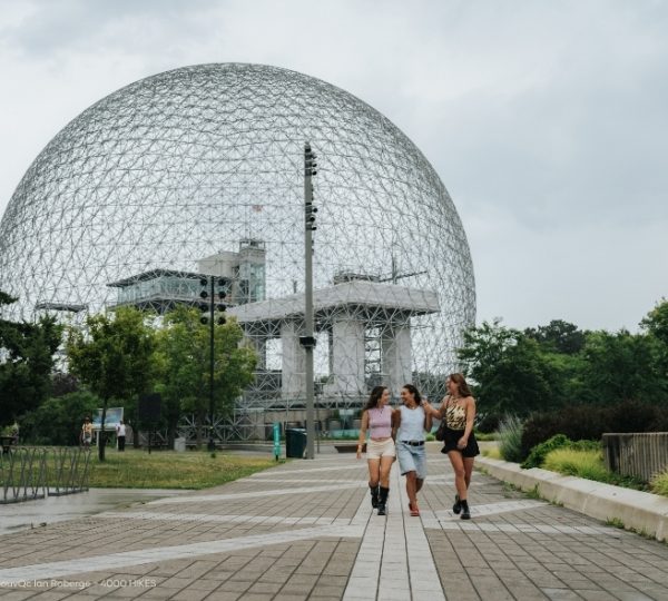Im Parc Jean-Drapeau in Montréal führt ein Spazierweg an einer großen geodätischen Kuppel vorbei, umgeben von grünen Bäumen und bewölktem Himmel. Kanada-Rundreise