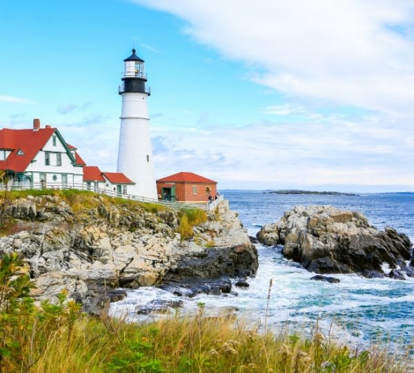 Portland, Maine – weißer Leuchtturm am felsigen Küstenstreifen, rotes Backsteinhaus, graue Felsen und blauer Himmel, Atlantik-Inselidyll Kanada-Rundreise