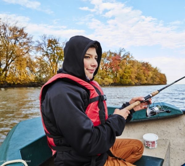 Beim Paddeln im Kajak: Eine Person mit schwarzer Kapuze und roter Jacke angelt auf türkisblauem Wasser, im Hintergrund herbstliche Bäume in Québec. Kanada-Rundreise