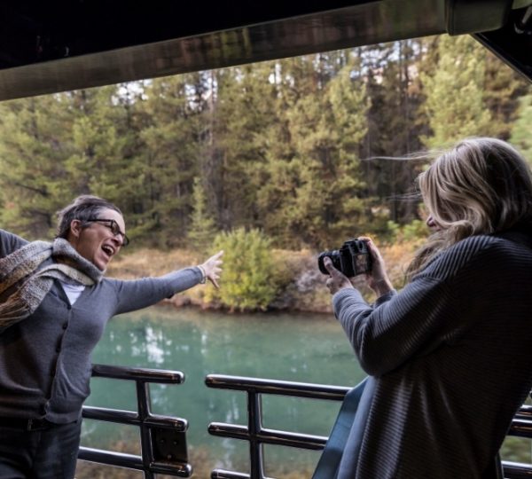 Im Zug bei Banff halten Reisende die Kamera ans Panoramafenster und erleben die Rocky Mountains mit türkisfarbenem Wasser und bewaldeten Bergen Kanada-Rundreise