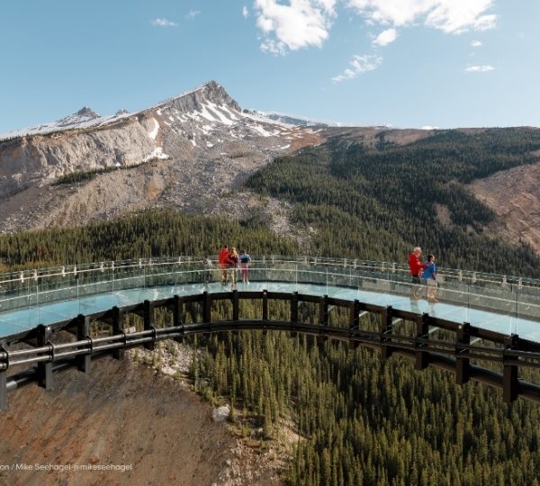 Besucher auf dem Columbia Icefield Skywalk stehen über einem türkisfarbenen Becken, umgeben von Fels- und Bergpanorama in Alberta bei Sonnenschein und Schluchten. Kanada-Rundreise