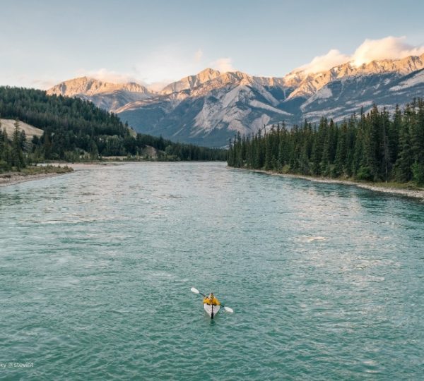 Ein türkisfarbenes Flussbett schlängelt sich durch den Nadelwald, während die Berge im Jasper Nationalpark im warmen Licht aufragen. Kanada-Rundreise