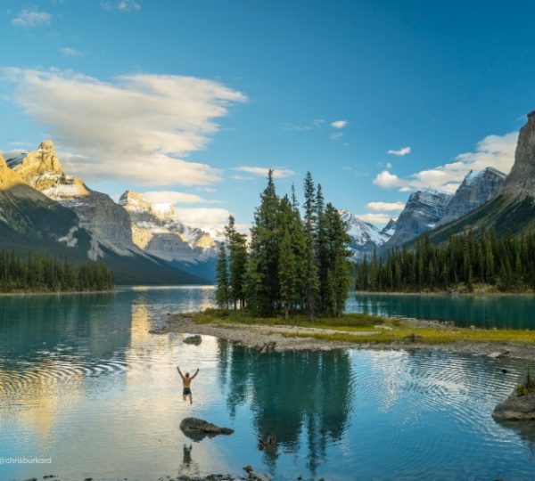 Ruhiger Blick auf den Maligne Lake mit türkisblauem Wasser, Nadelwald und schneebedeckten Bergen im Jasper Nationalpark, klarer Himmel Kanada-Rundreise