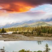 Über dem Jasper Nationalpark leuchten orange Wolken, während ein ruhiger Fluss vor bewaldeten Bergen liegt. Kanada-Rundreise