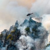 Ein Löschhubschrauber wirft Wasser über einen stark verrauchten, bewaldeten Hang im Fraser Canyon in British Columbia ab. Kanada-Rundreise