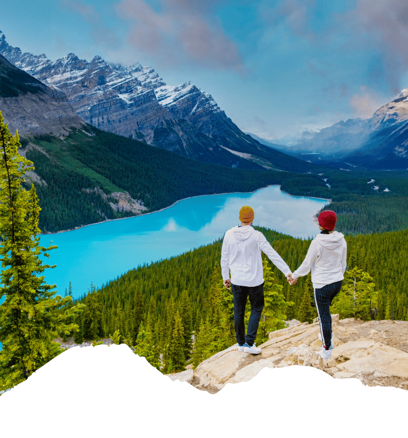 Zwei Wandernde halten sich an einem türkisblauen See in den kanadischen Rocky Mountains vor verschneiten Gipfeln an der Hand. Kanada-Rundreise