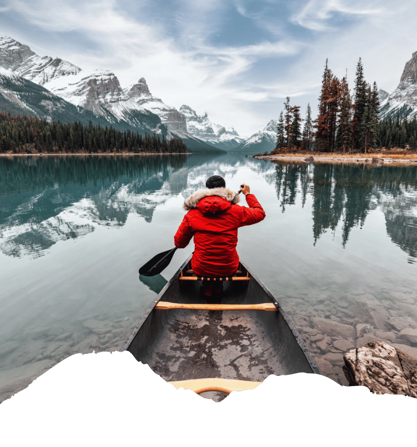 Eine Person in roter Jacke paddelt im Kanu über einen spiegelnden Bergsee vor schneebedeckten Rocky Mountains in Kanada. Kanada-Rundreise