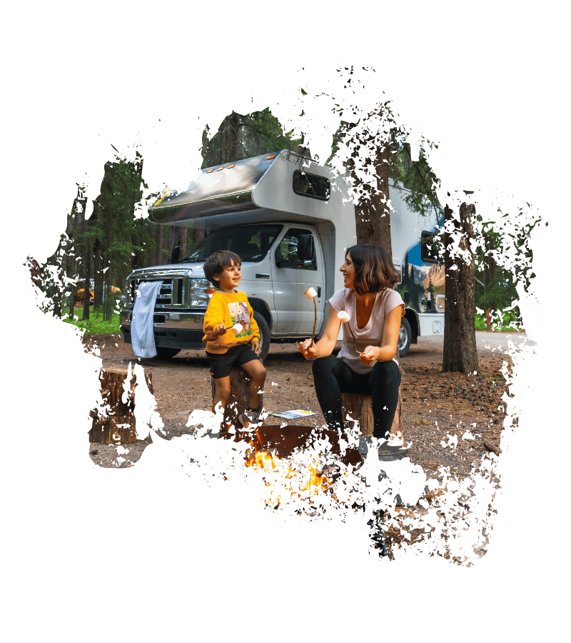 Eine Mutter sitzt mit ihrem Kind am Lagerfeuer vor einem mittleren Wohnmobil im kanadischen Wald. Kanada-Rundreise