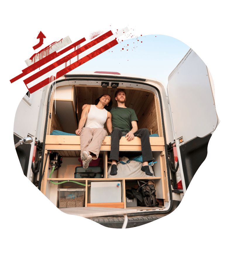 Ein Paar sitzt im ausgebauten Campervan auf dem Bett und zeigt den kompakten Innenraum mit Küche und Stauraum. Kanada-Rundreise