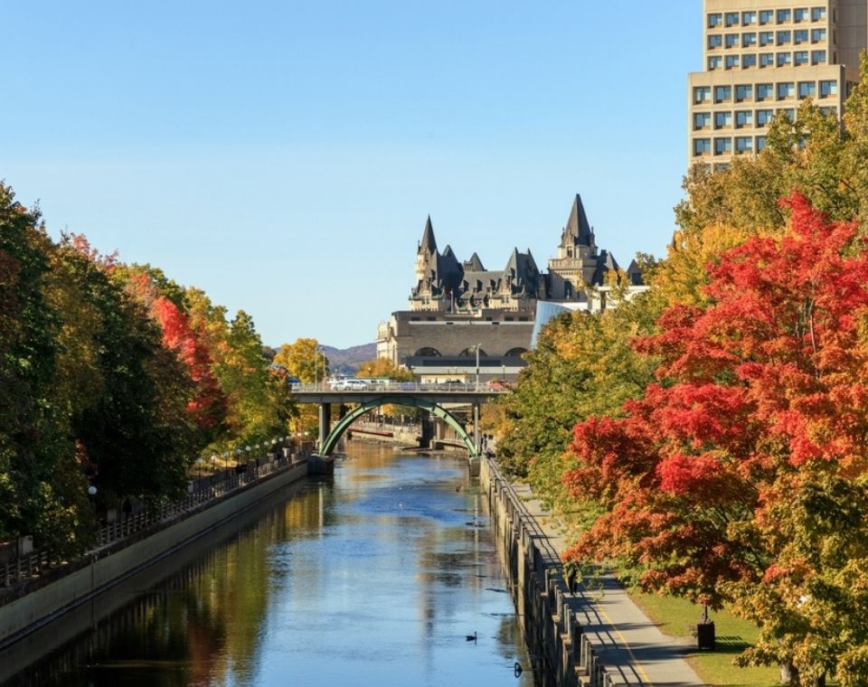 Herbstfarben säumen einen Kanal in Ottawa, während das Château Laurier und historische Brücken im Hintergrund zu sehen sind. Kanada-Rundreise